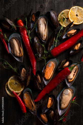 cooked mussels on a wooden background, the background is decorated with greens, pepper, microgreens, salt