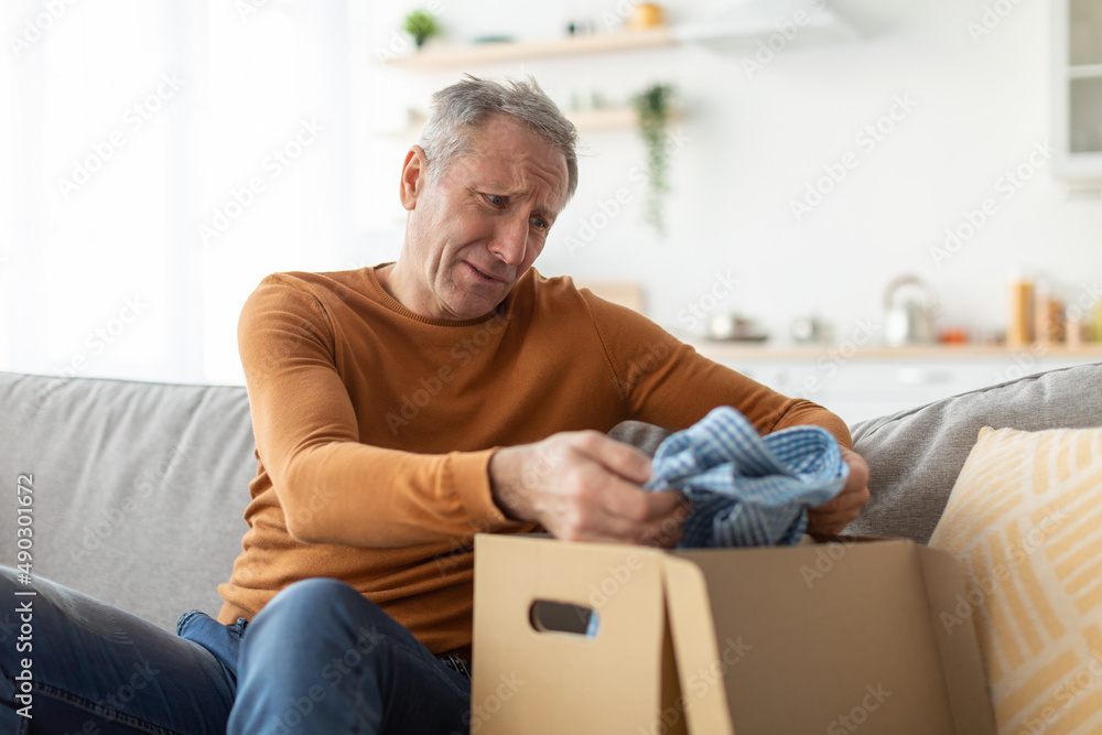 Sad mature man unpacking wrong parcel, delivery mistake concept Sad mature man unpacking wrong parcel, delivery mistake concept