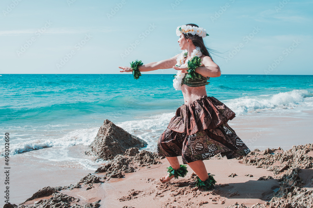 Woman with flower necklace on the beach.  Lady dancer dancing hula dance dressed in tropical outfit. Hawaiian woman enjoys hula dancing on the beach barefoot wearing traditional costume - obrazy, fototapety, plakaty 