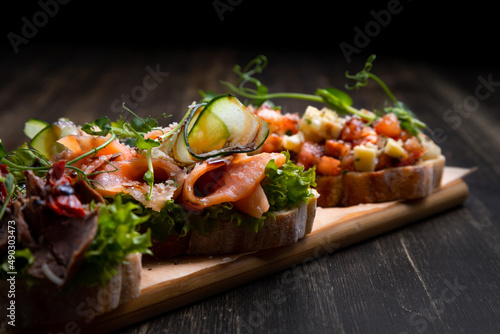 a dish of 3 different tapas stuffed with meat, fish and various microgreens, served on a board against a dark background