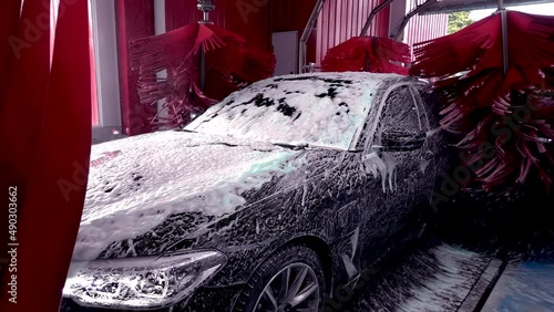 Black car moving though automatic car wash machine.Brush moving to clean the car. Slow motion shot