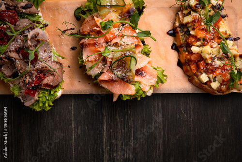 a dish of 3 different tapas stuffed with meat, fish and various microgreens, served on a board against a dark background