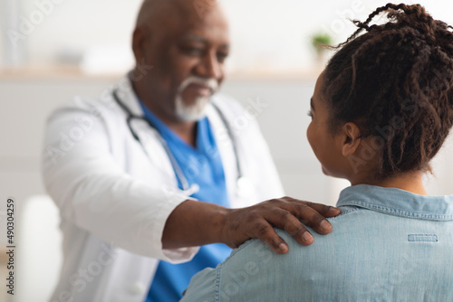 Close up of black male doctor tapping patting patient's shoulder