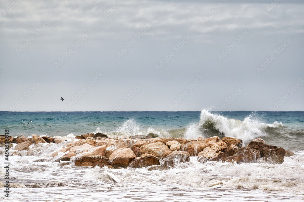 Sea waves crashing strongly against a breakwater near the shore of the beach on a day of rough seas and bad weather