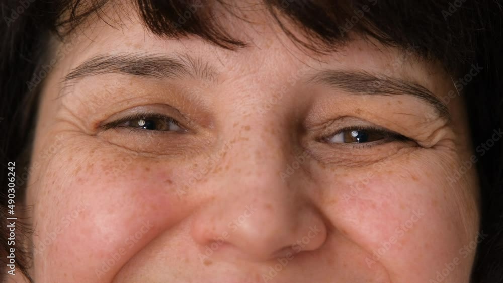 Face of happy elderly middle aged woman smiling with friendly eyes. Handsome mature female senior citizen with wrinkles on attractive face looking and laughing at camera. Macro extreme close up Face of happy elderly middle aged woman smiling with friendly eyes. Handsome mature female senior citizen with wrinkles on attractive face looking and laughing at camera. Macro extreme close up