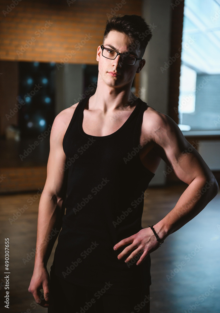 Handsome friendly athlete or personal trainer in gym. Young sporty man smiling standing on fitness club background