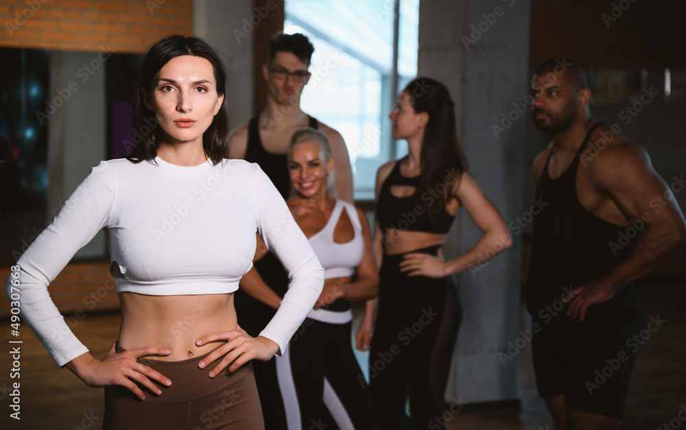 Group of happy smiling muscular sports fitness female and male adults people standing together as good friends in gym with sport equipment in background after a difficult workout session