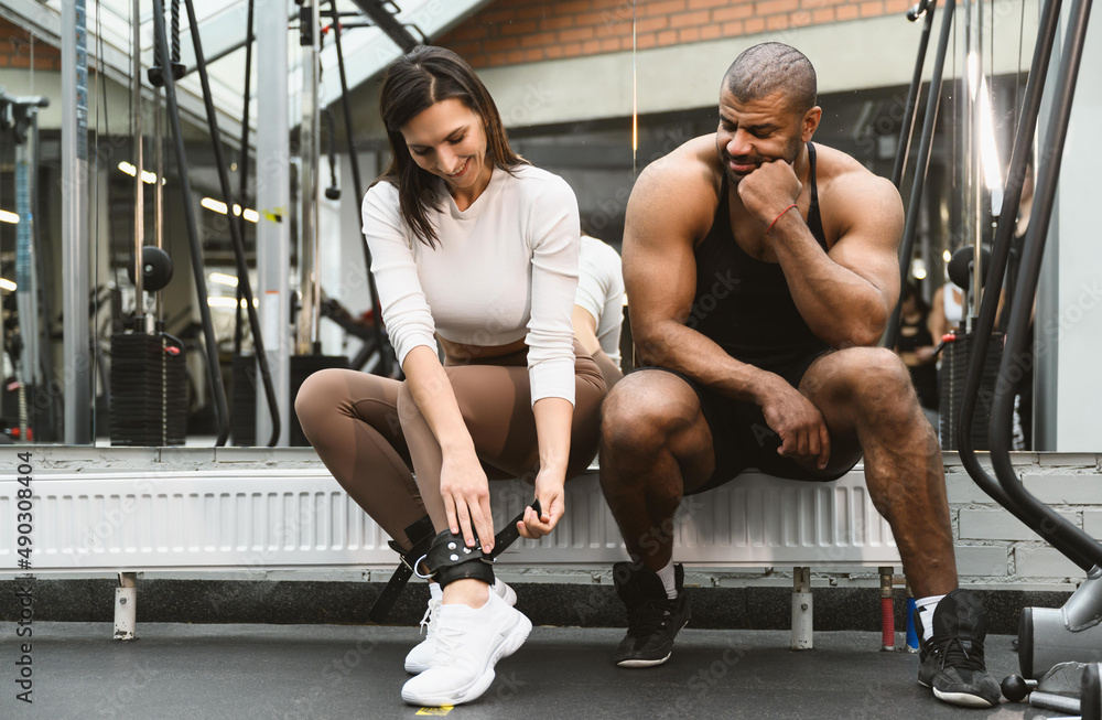 A young woman is preparing for training in the crossover simulator. Personal trainer afro american man teaches how to do the exercise correctly A young woman is preparing for training in the crossover simulator. Personal trainer afro american man teaches how to do the exercise correctly