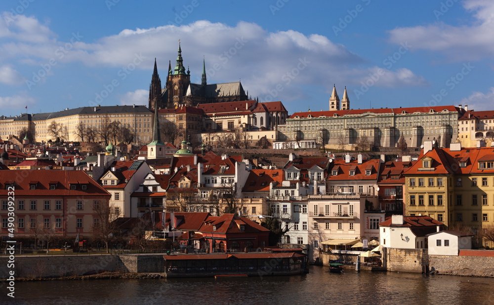 Prague Castle and its neighborhood. The cathedral the castle and the historic districts all around under the sun. The sky has a few clouds.