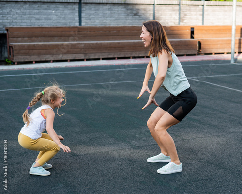 Mother and daughter go in for sports outdoors. Caucasian woman and little girl are engaged in fitness at the stadium.