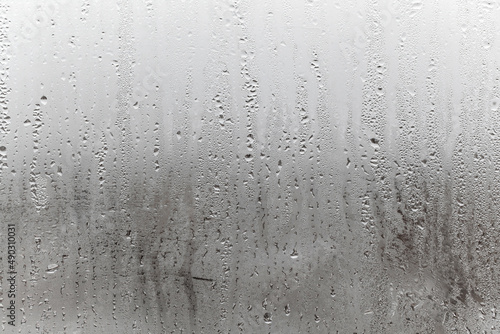 Steamy window with water drops made in dull day, condensation on glass with drops flowing down, humidity and foggy blank