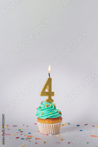 Homemade cupcake with colorful sprinkles and a candle in the shape of the number four on a white background.