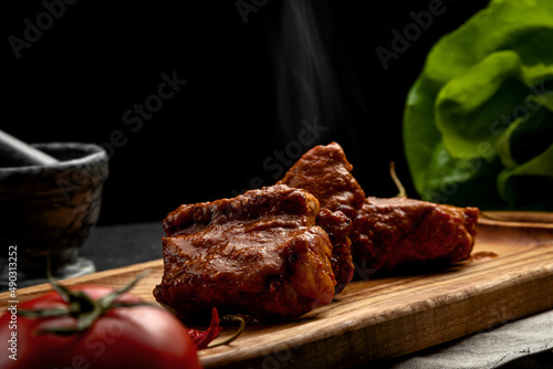 spicy ribs served on a board with hot chili peppers, on a dark background