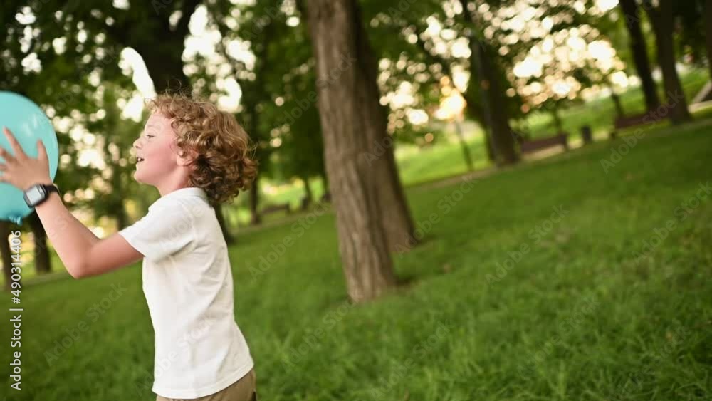 baby boy with curly hair and glasses playing with a blue balloon on the background of greenery and park baby boy with curly hair and glasses playing with a blue balloon on the background of greenery and park