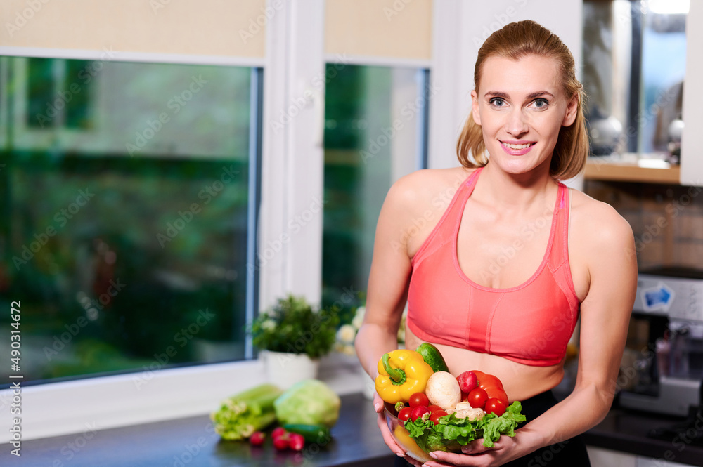Fitness Girl in sport wear holds Vegetable Salad Standing Over kitchen Background Fitness Girl in sport wear holds Vegetable Salad Standing Over kitchen Background