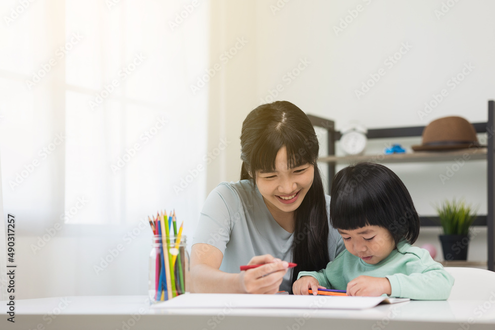 Happy asian boy painting with crayon and colored pencil with his mother in living room at home. Mom teaching son how to painting with crayon color on book or doing homework. family concept. Happy asian boy painting with crayon and colored pencil with his mother in living room at home. Mom teaching son how to painting with crayon color on book or doing homework. family concept.