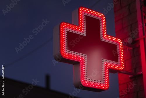 A red lit pharmacy cross against dark cloudy in the evening
