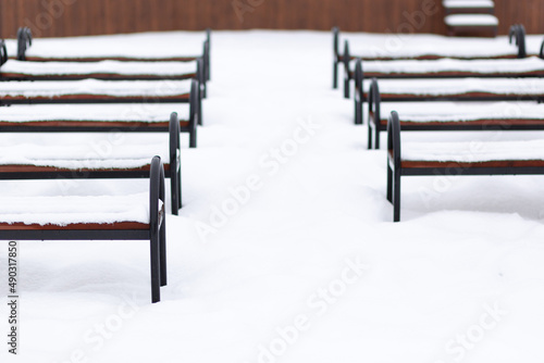 A row of benches covered with snow. Top view. Wooden and steel benches in the park