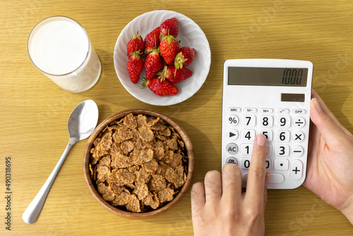 手と電卓と朝食（フレーク、苺、牛乳）。食費のイメージ photo