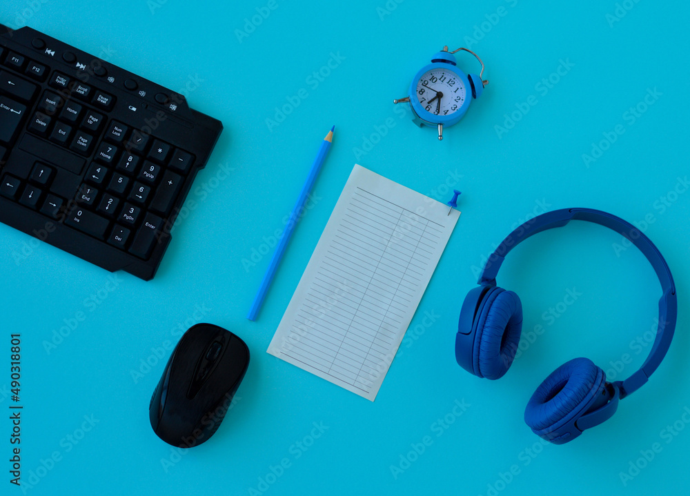 Flat lay home office desk. Workspace with laptop, headphones, pencil, alarm clock and a piece of paper for notes on blue background. Top view feminine background. Flat lay home office desk. Workspace with laptop, headphones, pencil, alarm clock and a piece of paper for notes on blue background. Top view feminine background.