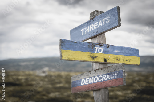 threaths to democracy text quote on wooden signpost outdoors on nato colored flag, ukrainian flag and russian flag. © Jon Anders Wiken