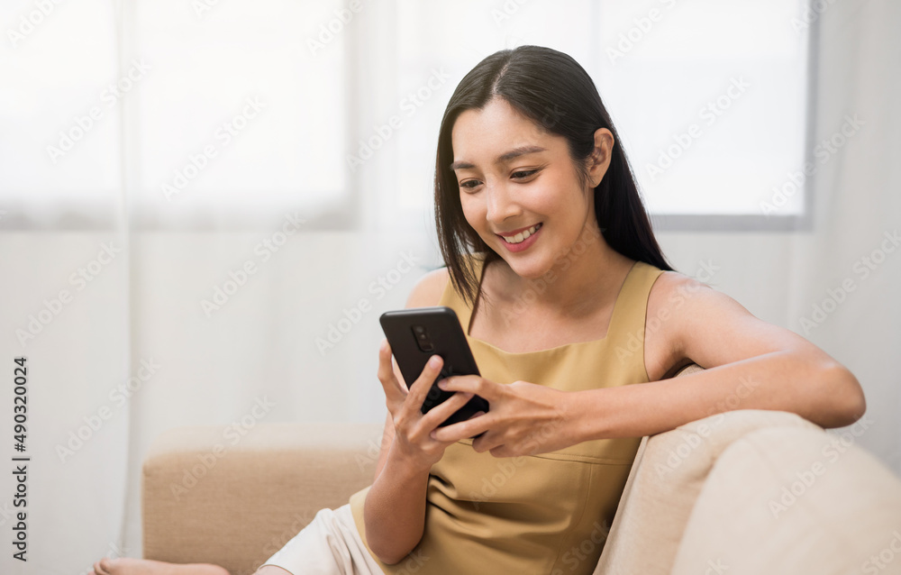 Asian woman using smartphone. Chatting video conference online sitting sofa in living room at home. Business Woman Shopping online store. Relax time at home Asian woman using smartphone. Chatting video conference online sitting sofa in living room at home. Business Woman Shopping online store. Relax time at home
