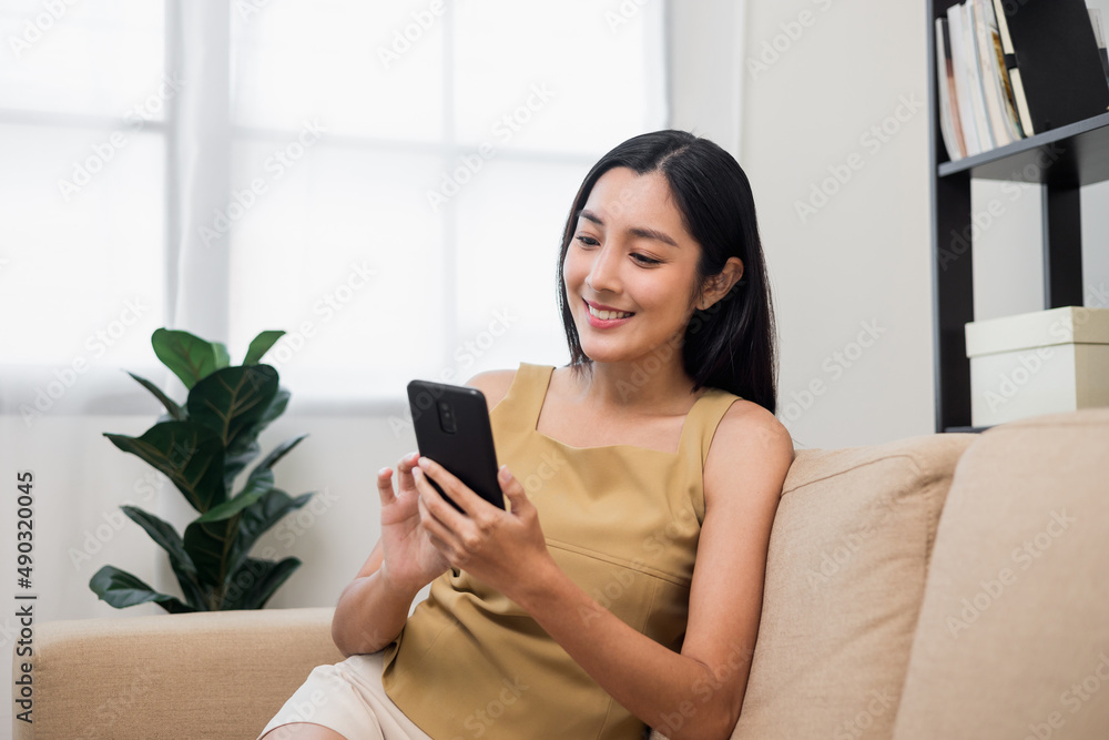 Asian woman using smartphone. Chatting video conference online sitting sofa in living room at home. Business Woman Shopping online store. Relax time at home Asian woman using smartphone. Chatting video conference online sitting sofa in living room at home. Business Woman Shopping online store. Relax time at home