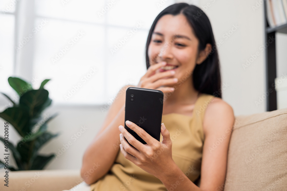 Asian woman using smartphone. Chatting video conference online sitting sofa in living room at home. Business Woman Shopping online store. Relax time at home Asian woman using smartphone. Chatting video conference online sitting sofa in living room at home. Business Woman Shopping online store. Relax time at home