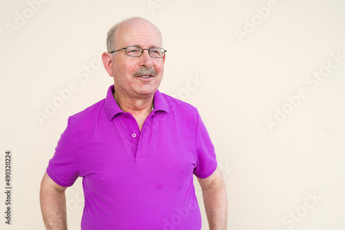 Portrait of happy senior man thinking and standing against plain background