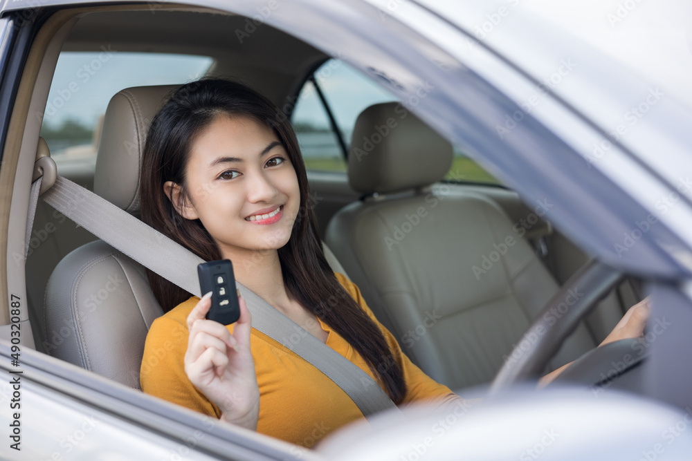 Young beautiful asian women getting new car. she very happy and excited looking outside window in hand holding car key. Smiling female driving vehicle on the road on a bright day Young beautiful asian women getting new car. she very happy and excited looking outside window in hand holding car key. Smiling female driving vehicle on the road on a bright day