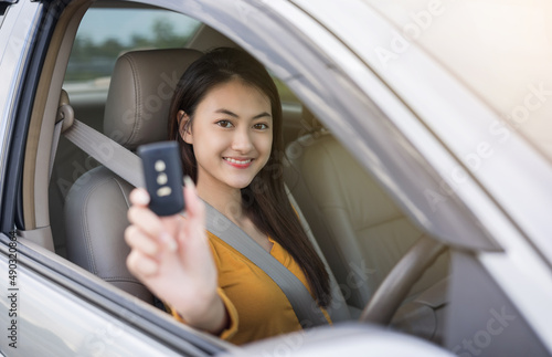 Young beautiful asian women getting new car. she very happy and excited looking outside window in hand holding car key. Smiling female driving vehicle on the road on a bright day