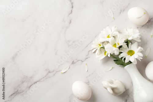 Top view photo of the white vase with bouquet of chrysanthemum figure of rabbit and few eggs on isolated marble empty background