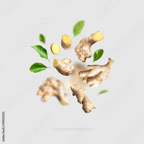 Fototapeta Flying fresh ginger root, green leaves isolated on gray background