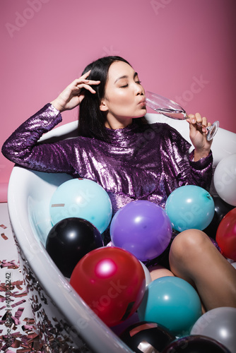 Wall Mural asian woman in purple dress lying in bathtub with colorful balloons and drinking