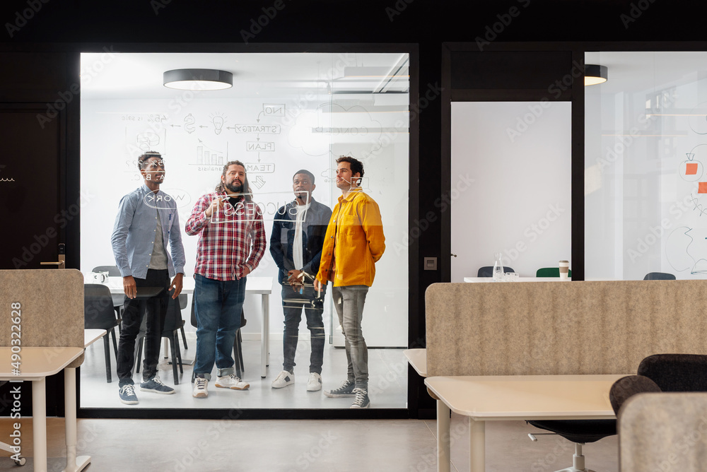 Fototapeta premium multiracial group of coworkers work in an office room drawing on a glass wall strategies for the success of the company. Brainstorming session.