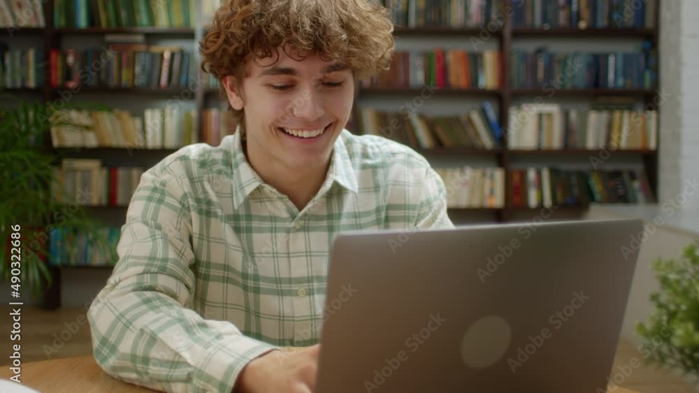 Attractive Student Man Looking at Laptop Monitor Doing Research and Smile. Young Male Professional Using Computer and Smile Sitting at Home Office or Library. Busy Worker Freelancer Working on Tech Attractive Student Man Looking at Laptop Monitor Doing Research and Smile. Young Male Professional Using Computer and Smile Sitting at Home Office or Library. Busy Worker Freelancer Working on Tech