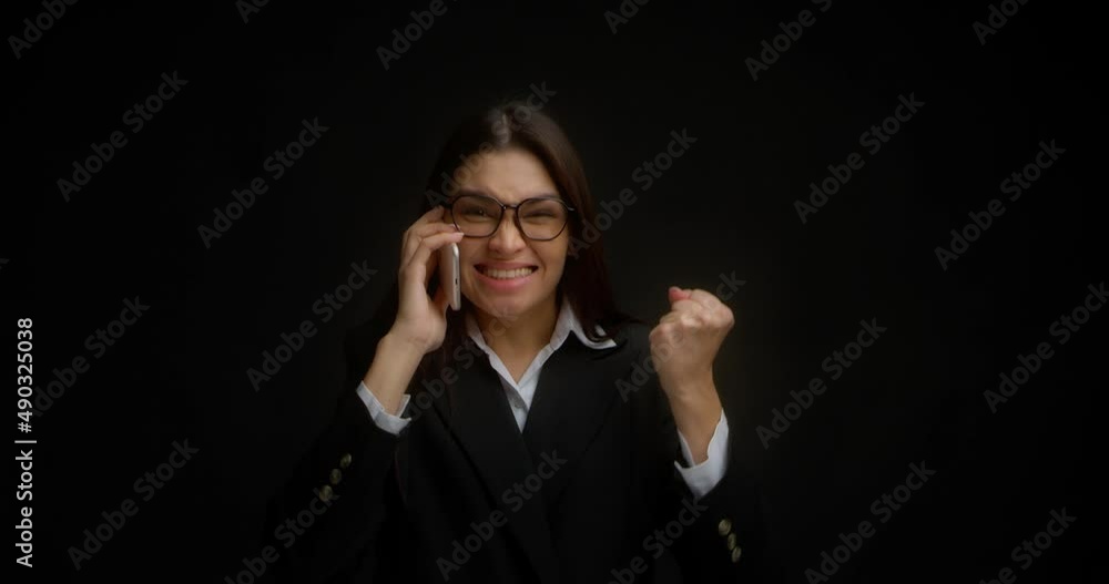 Business woman with glasses is glad to hear pleasant news in a telephone conversation. Beautiful brunette in a business suit rejoices at a successful deal, shows an affirmative gesture with her hands Business woman with glasses is glad to hear pleasant news in a telephone conversation. Beautiful brunette in a business suit rejoices at a successful deal, shows an affirmative gesture with her hands
