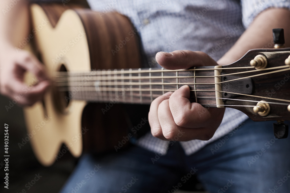 Practice makes perfect. Cropped shot of an unrecognizable man playing an acoustic guitar at home.
