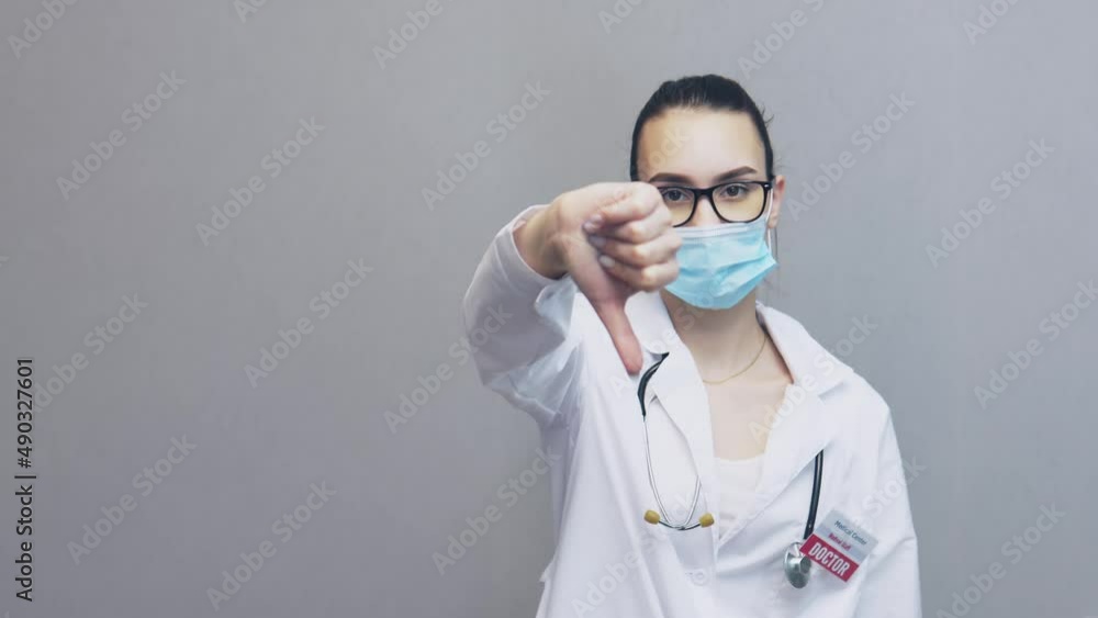 woman female doctor in uniform, glasses, facial mask showing thumb down sign. pretty young caucasian professional medical physician in white lab coat, stethoscope over neck, gesturing, thumbs up, woman female doctor in uniform, glasses, facial mask showing thumb down sign. pretty young caucasian professional medical physician in white lab coat, stethoscope over neck, gesturing, thumbs up,
