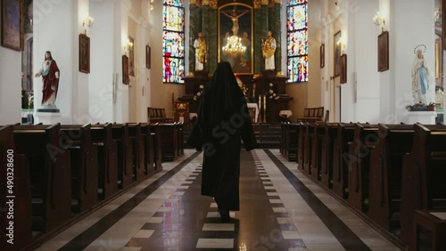 Nun walking inside a catholic church toward the sacred altar seen from behind, religious people concept photo