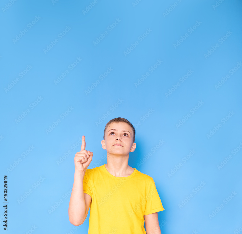 Portrait of a cheerful boy pointing at the top with his finger - isolated on a blue background Portrait of a cheerful boy pointing at the top with his finger - isolated on a blue background