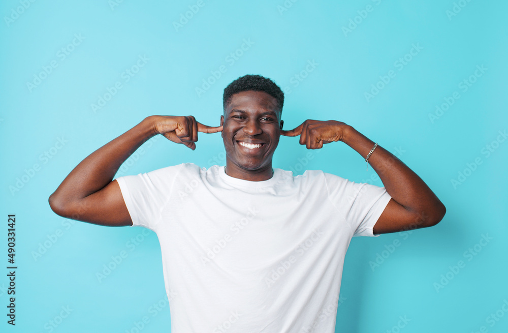 a handsome American guy in a white T-shirt covers his ears with his fingers on a blue isolated background. a handsome American guy in a white T-shirt covers his ears with his fingers on a blue isolated background.