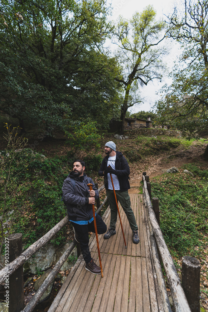 Dos amigos hombres en un puente de madera durante una ruta verde hablando
