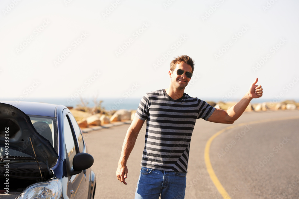Hes hitching a ride. A handsome young man standing on the side of the road besides his broken-down car and hitching a ride. Hes hitching a ride. A handsome young man standing on the side of the road besides his broken-down car and hitching a ride.