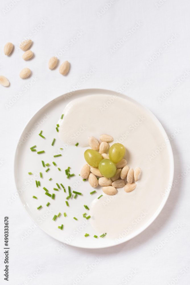 Crema de almendras, sopa fría española. Ajo blanco de Málaga con almendras y uvas en un recipiente blanco sobre una mesa blanca. Vista superior Crema de almendras, sopa fría española. Ajo blanco de Málaga con almendras y uvas en un recipiente blanco sobre una mesa blanca. Vista superior