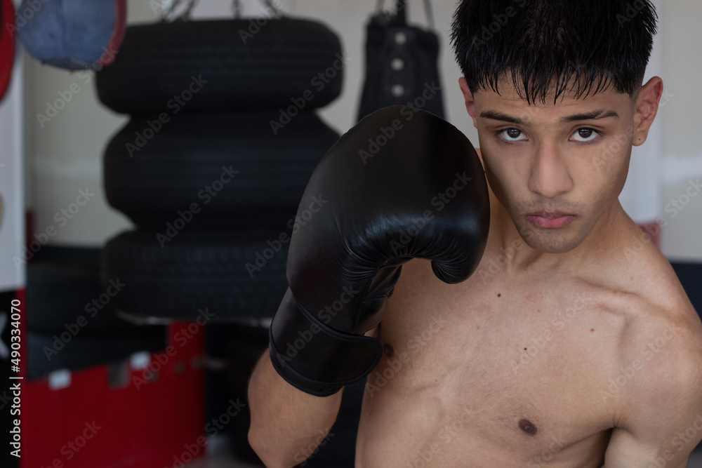 young, shirtless Latino boxer wearing black gloves, with his fist covering one side of his face