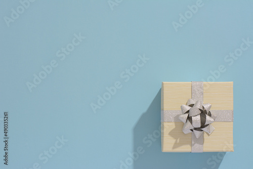 One BEIGE gift box with silver ribbon and bow on light blue table background. Minimal festive gift background. Top view. Flat lay.	
