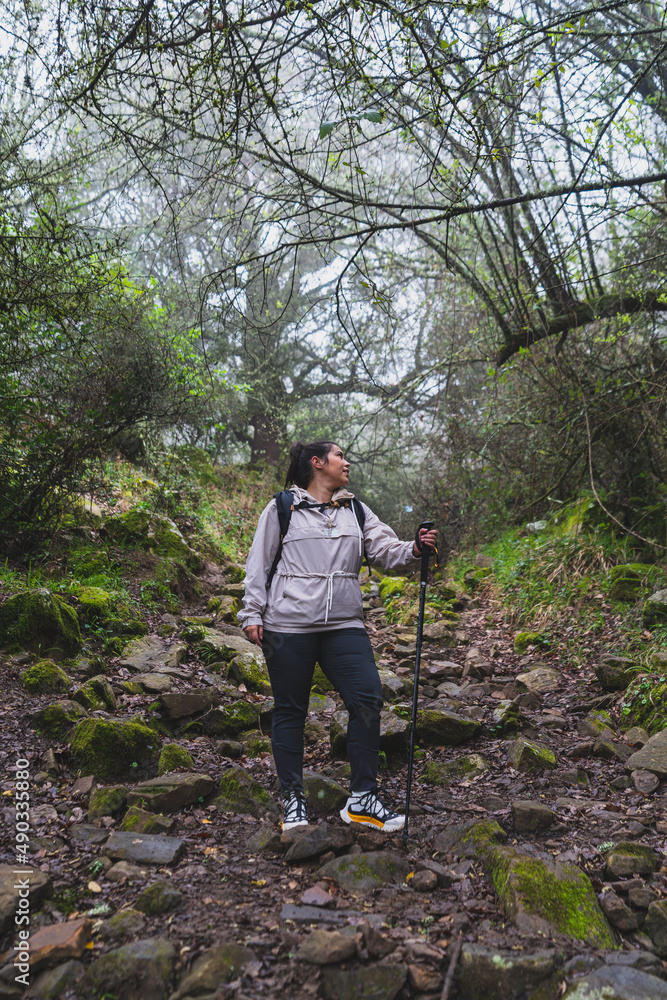 Chica joven guapa en mitad de sendero de un bosque con niebla realizando senderismo