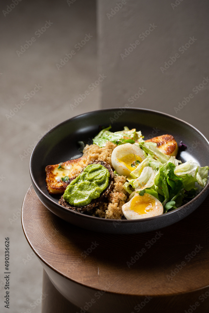 Plate with breakfast salads: avocado toast, egg, greens, fried cheese, quinoa Plate with breakfast salads: avocado toast, egg, greens, fried cheese, quinoa