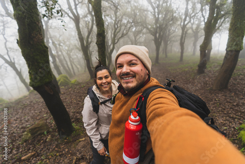 Selfie de una pareja joven en un bosque haciendo senderismo con niebla por los arboles photo